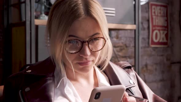 Portrait Of A Business Woman Blonde With Glasses Looking Down Using A Smartphone  alt