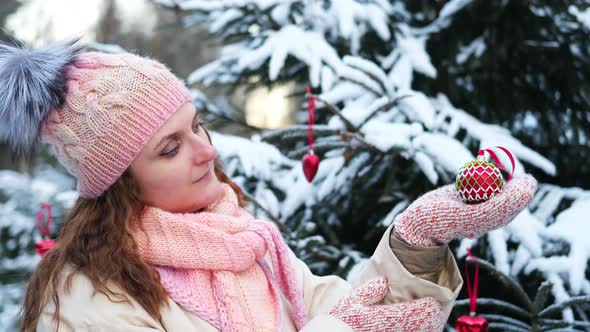 Happy woman looks at Christmas tree toy in winter forest alt