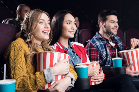 young smiling friends with popcorn watching film in movie theater