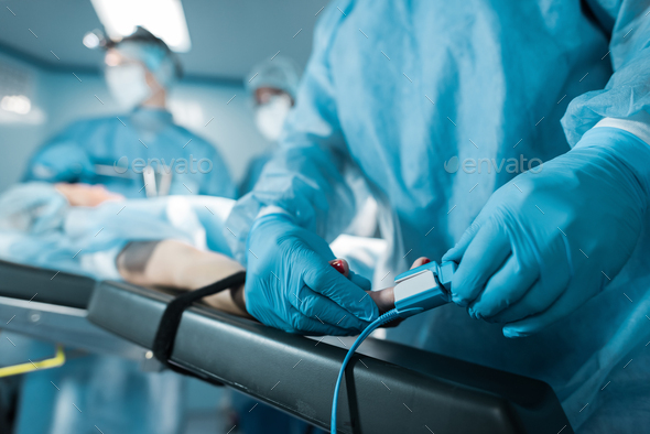 cropped image of doctor wearing pulse oximeter on patient finger in operating room