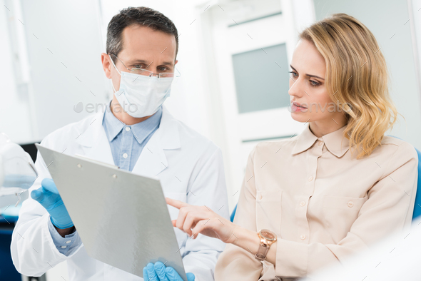 Doctor and smiling patient looking at diagnosis records in modern dental clinic