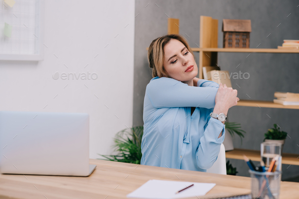 attractive businesswoman stretching shoulders at workplace in office