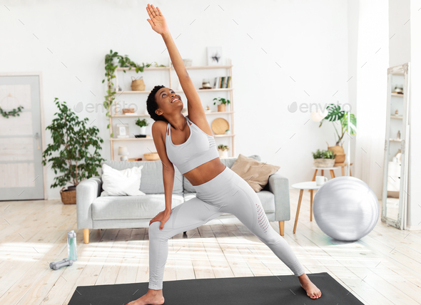 Fit black woman stretching her body on yoga mat during her home workout  Stock Photo by Prostock-studio