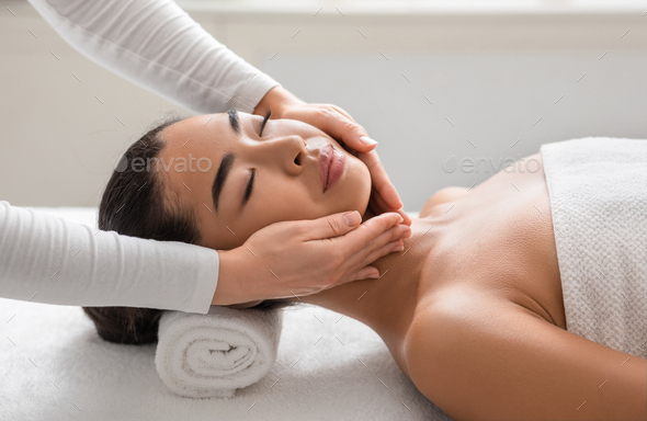 Facial beauty treatment. Asian woman getting face lifting massage at cosmetology cabinet