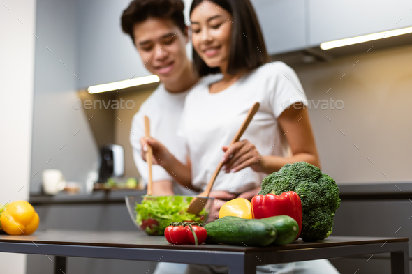 Asian Couple Cooking In Kitchen, Focus On Vegetables On Table