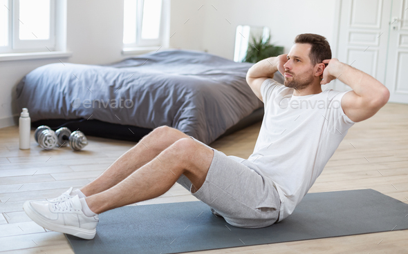 Sporty Man Doing Sit Ups Abs Exercise On Mat In Bedroom