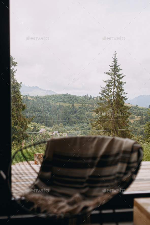 Beautiful view on mountains hills and trees through window cabin. Blurred chair with cozy blanket