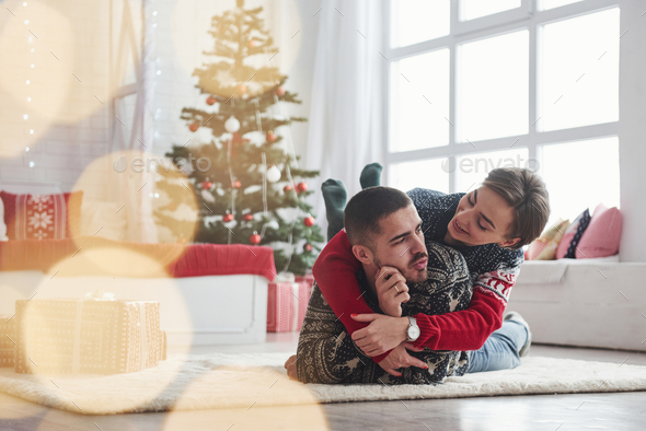 Lovely young couple lying on the living room with green holiday tree at background