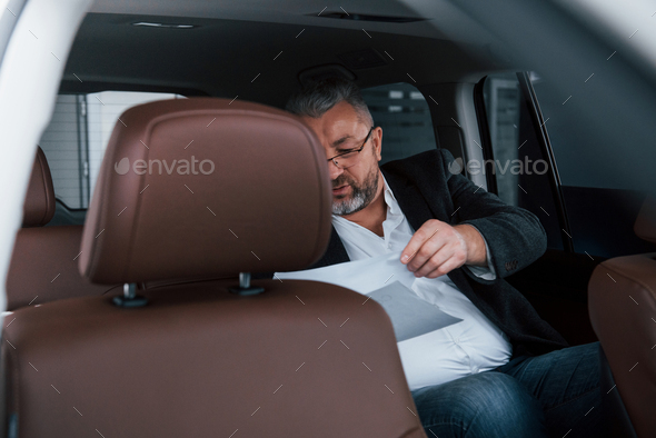 Reading contract. Paperwork on the back seat of the car. Senior businessman with documents
