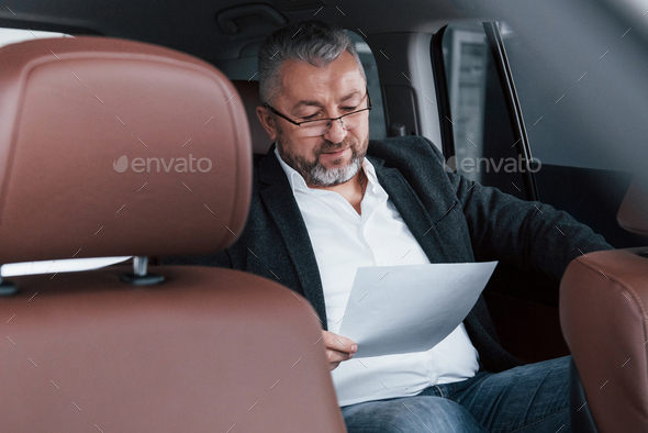 Paperwork on the back seat of the car. Senior businessman with documents