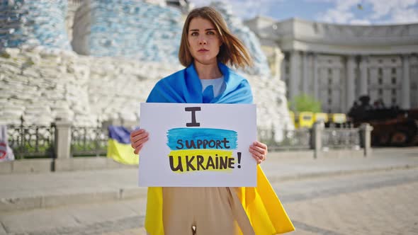 Woman Holds Placard Against Monuments Covered with Sandbags alt