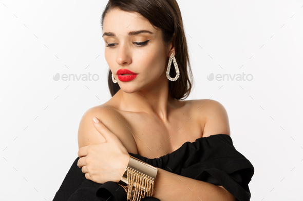 Fashion and beauty concept. Elegant woman with red lips, black dress, showing earrings and jewelry - Stock Photo - Images