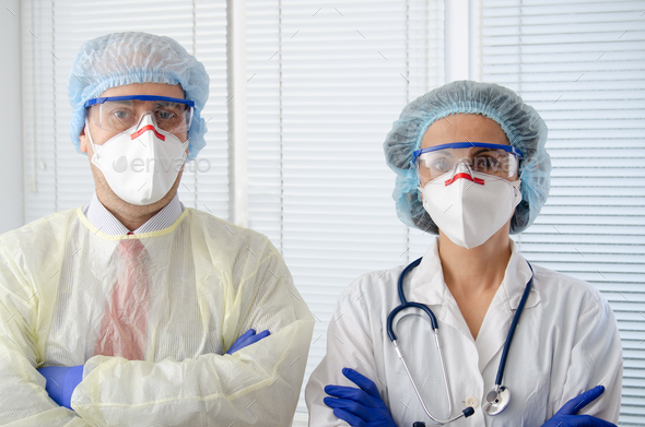 Male and female health care workers in masks glasses caps and gloves standing with arms crossed - Stock Photo - Images