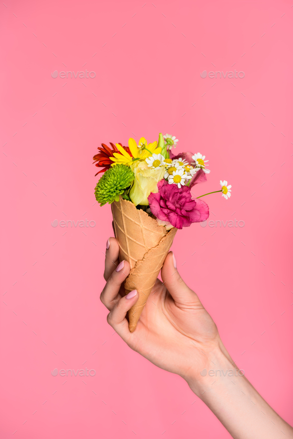 close-up partial view of woman holding ice cream cone with beautiful flowers isolated on pink