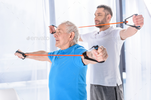 selective focus of rehabilitation therapist and senior man exercising with rubber tapes