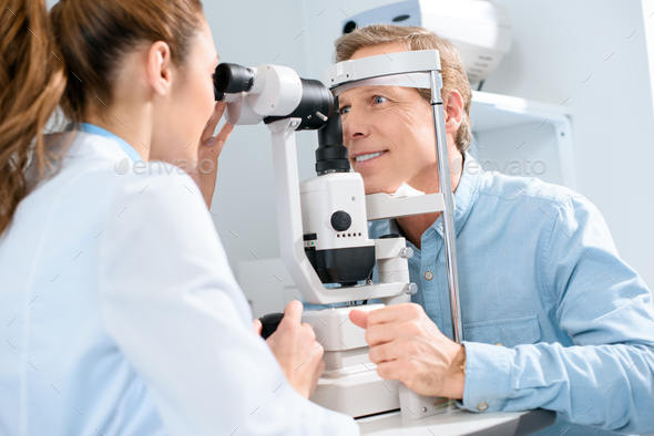professional female optician examining man with modern visual equipment