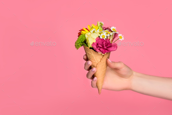 cropped shot of girl holding ice cream cone with beautiful flowers isolated on pink