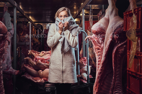 A woman in a warm jacket in a meat freezer storage.