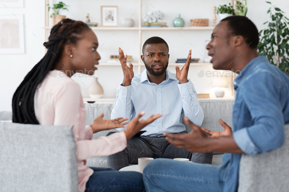Annoyed black psychologist watching couple arguing during marital therapy session