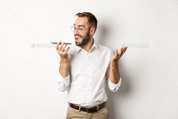 Excited businessman talking on speakerphone and smiling, record voice message with ecstatic face