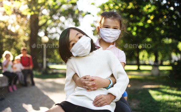 Small school girls with face mask on playground outdoors in town, coronavirus concept.