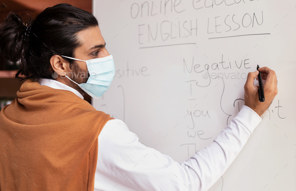 Teacher In Mask Teaching English Grammar Writing On Blackboard Indoors