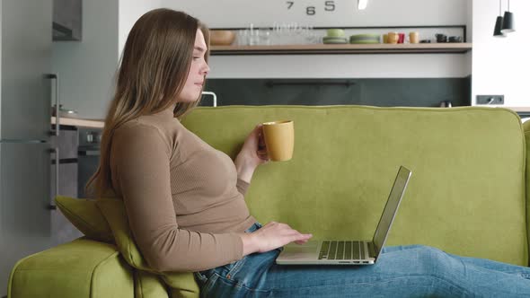 Beautiful Attractive Woman Using Laptop Lying on Sofa and Frinking Hot Coffee or Tea When Relax in alt