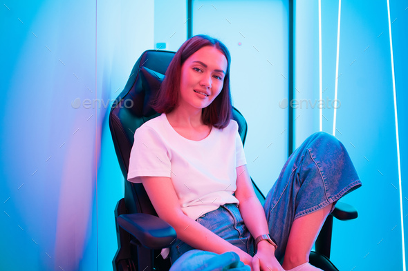 Streamer girl relaxing sitting on a gaming chair after live stream. Room with colorful neon light