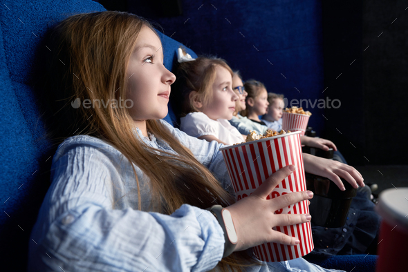 Side view of pretty girl watching film in cinema