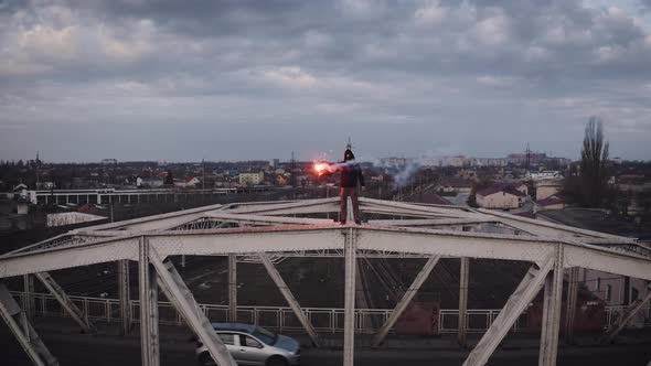 Aerial View of Young Man in Hoodie and Balaclava Standing on the Top of the Frame Construction of an alt