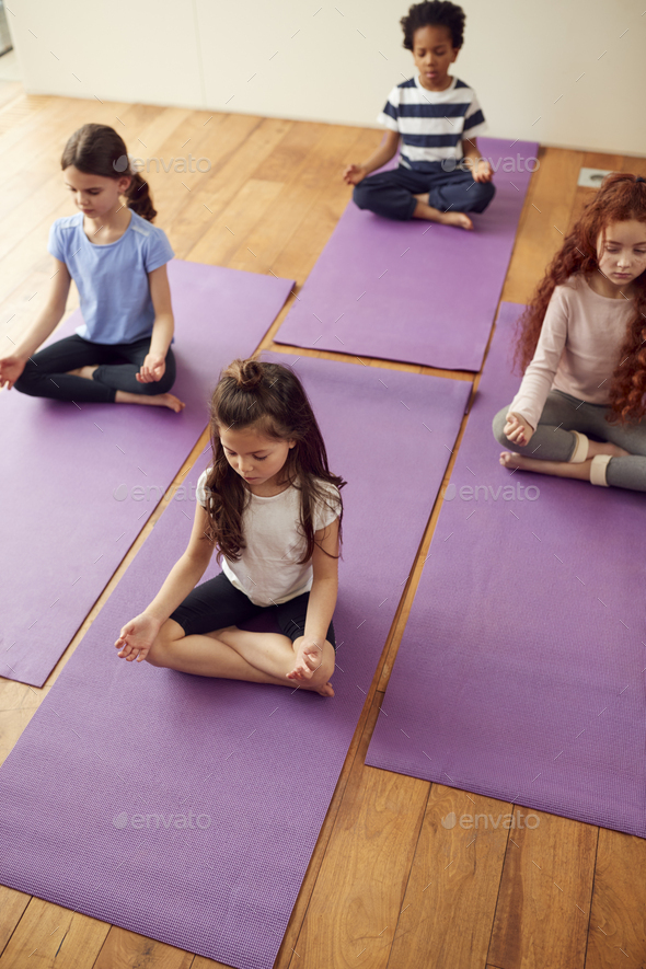 Group Of Children Sitting On Exercise Mats And Meditating In Yoga Studio  Stock Photo by monkeybusiness