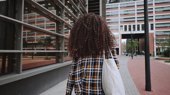Back View of African American Girl with Curly Hair in Card Shirt is Going Home From the University alt