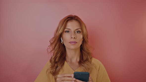 Blonde Pinup Style Girl Inserts Headphones in Her Ears and Dances on a Pink Background alt