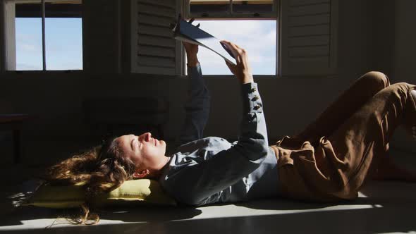 Caucasian woman lying on floor holding book and reading in sunny cottage living room alt