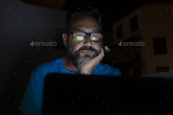 Stressed and worried man work by night on laptop computer - online social media life and stress