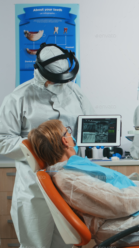 Dentist in coverall examining x-ray image on tablet