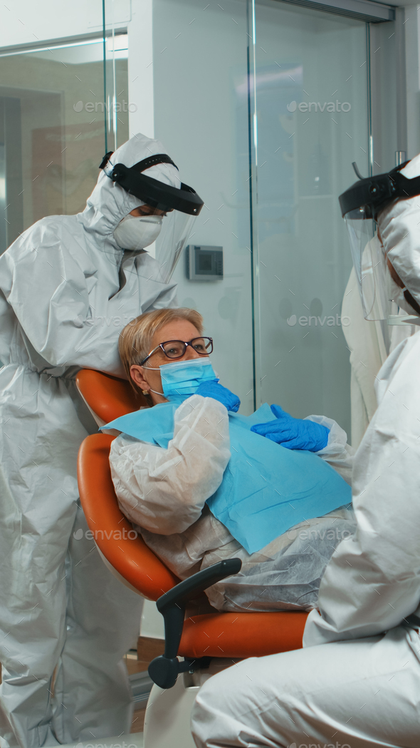 Nurse in coverall putting dental bib to woman during examining