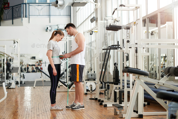 Fitness trainer measuring waist of female client