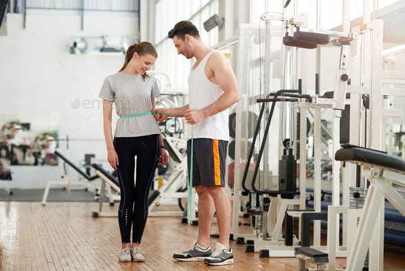 Personal trainer measuring a woman waist at the fitness club