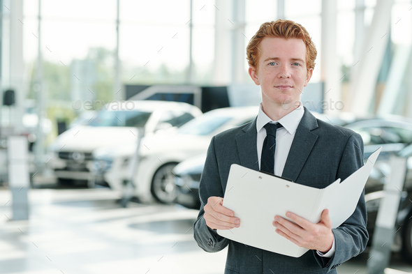 Young serious manager of contemporary car center holding open folder