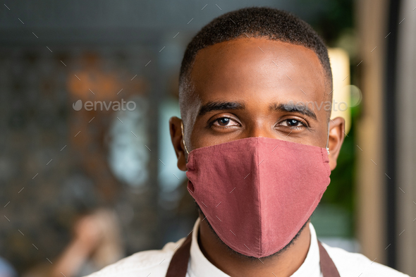 Head of young contemporary waiter of African ethnicity in protective mask