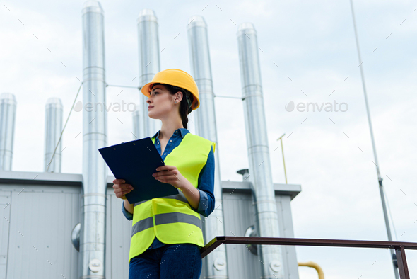 Download Beautiful Female Builder In Safety Vest And Hardhat Writing In Clipboard On Industrial Construction Stock Photo By Lightfieldstudios