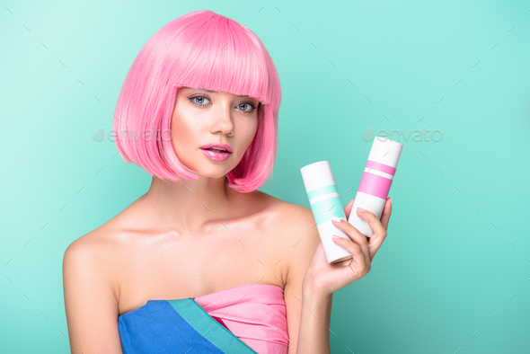 attractive young woman with pink bob cut holding cans of coloring hair sprays isolated on turquoise