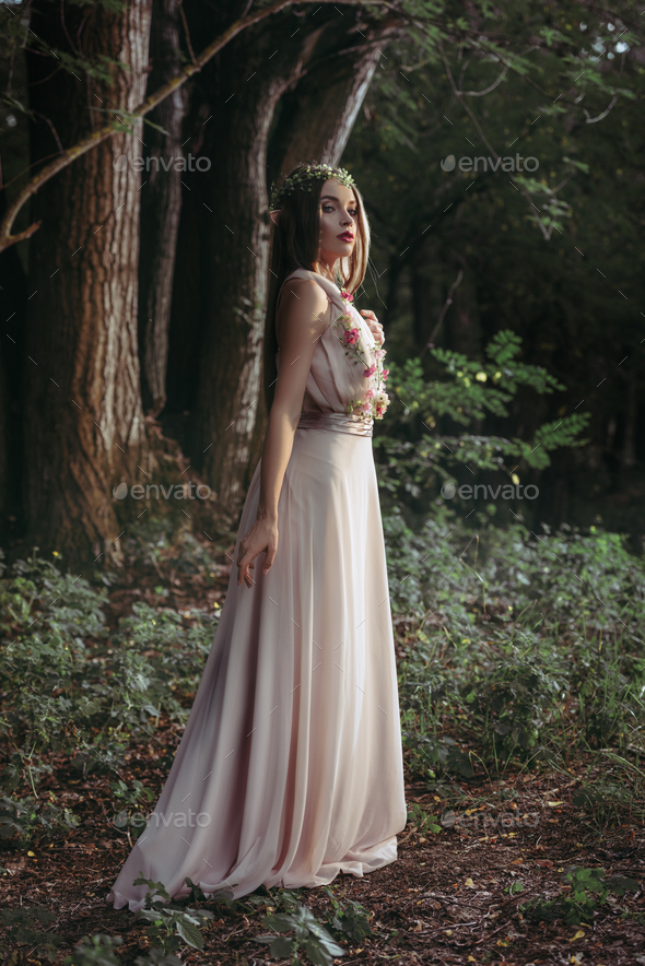 elegant mystic elf in flower dress posing in dark woods