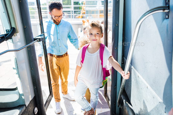 schoolgirl entering school bus with teacher while going on excursion