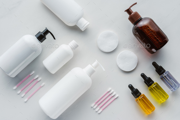 top view of bottles of cream, natural oils and cosmetic pads on white surface, beauty concept