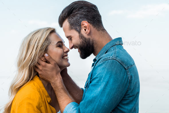 side view of smiling couple hugging and going to kiss against blue sky - Stock Photo - Images