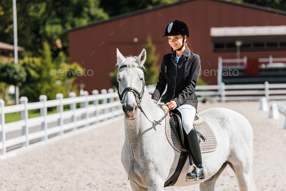 attractive smiling female equestrian riding horse at horse club