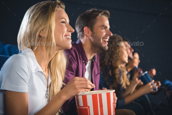 cheerful friends with popcorn watching film together in movie theater