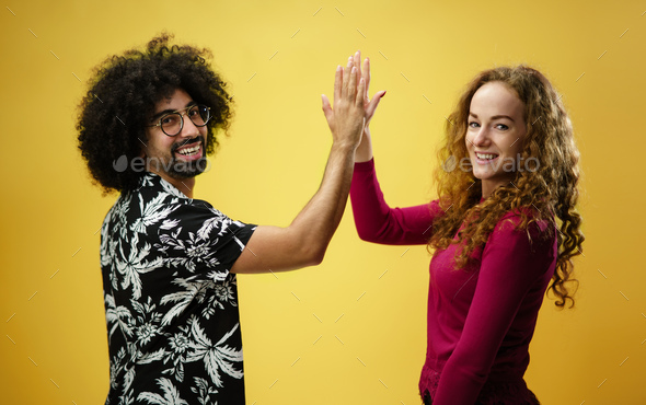 Mature man and young woman in a studio on yellow background, giving high  five. Stock Photo by halfpoint